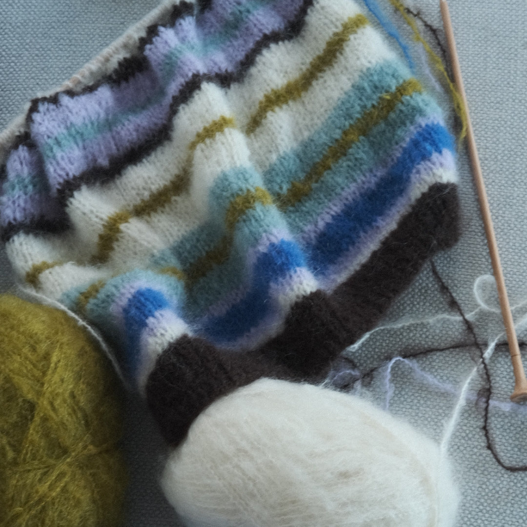 Knitted fabric with colorful stripes next to yarn balls on a textured surface