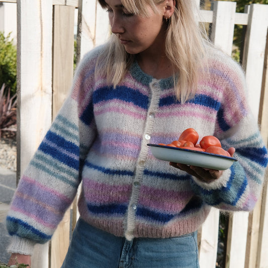 Person wearing a colorful striped sweater holding a plate of tomatoes outdoors.