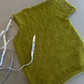 Green knitted sweater on a light gray surface with a measuring tape.