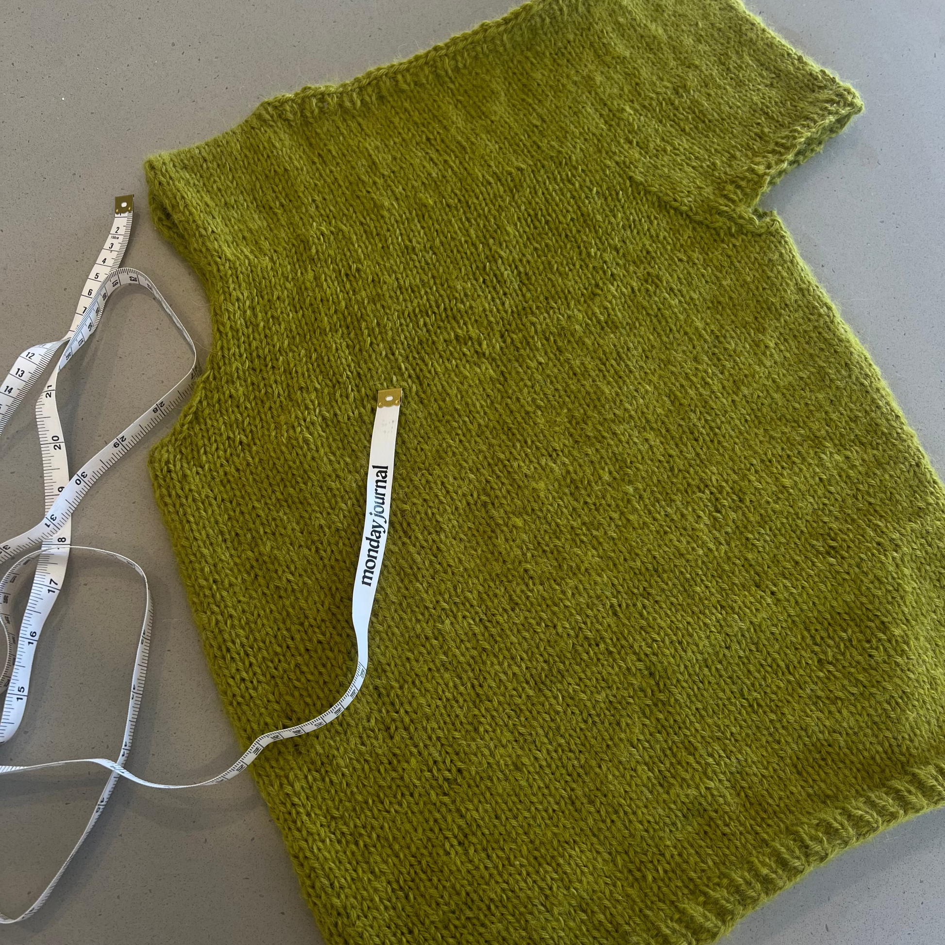 Green knitted sweater on a light gray surface with a measuring tape.