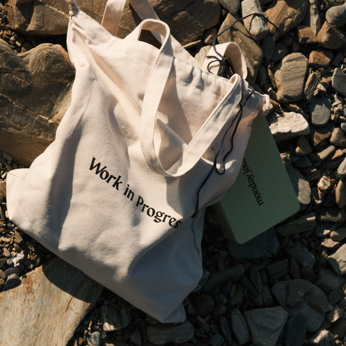 White tote bag with 'Work in Progress' text on a rocky surface